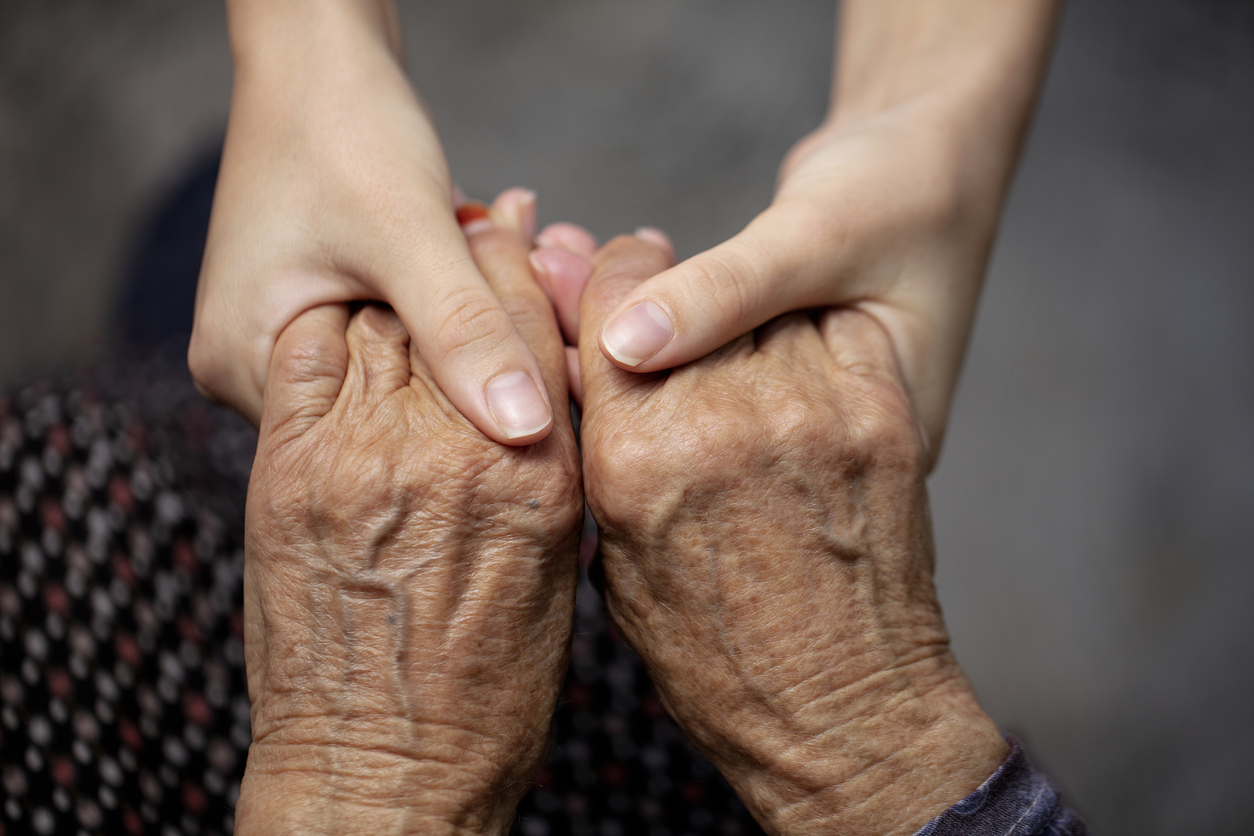Younger hands gently clasping an aging parent's hands in a moment of support and reassurance