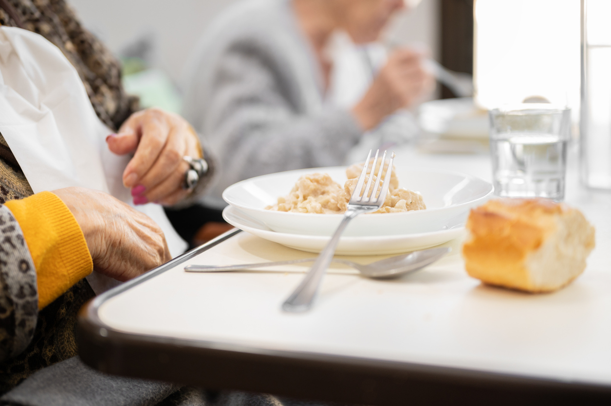 Senior woman enjoying a chef-prepared meal in the dining room of an assisted living community.